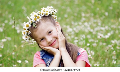 On A Chamomile Lawn, A Sweet Girl In A Wreath Of Daisies, Smiling, Pressing Her Hands To Her Cheeks. High Quality Photo