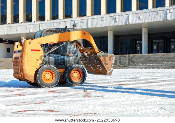 On a clear winter day, a\
manoeuvrable grader clears snowdrifts from the city square in front\
of the facade of the administrative building. Copy\
space.