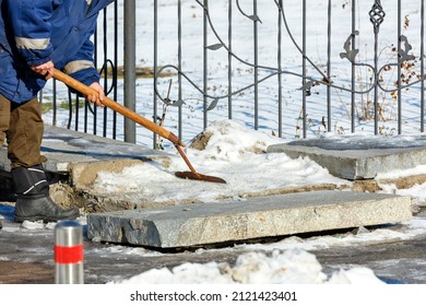 On A Clear Winter Day, A Utility Worker Clears Snow And Ice From A Granite Curb On A City Street.