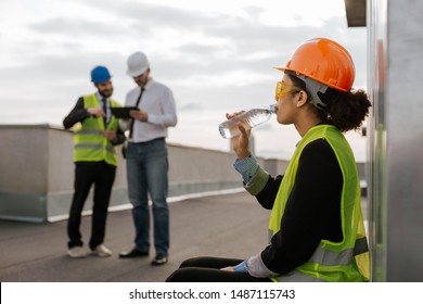 On Construction Site Beautiful Smiling African Lady Engineer Drinking Some Water From Bottle On The Rooftop Of Building She Wearing Safety Helmet And Yellow Safety Glasses