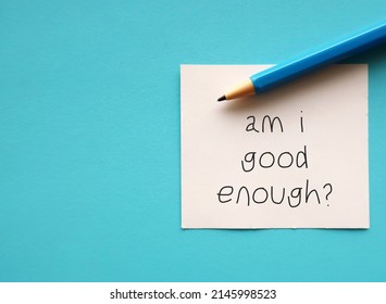 On copy space blue background, pen and note AM I GOOD ENOUGH? - negative self talk showing self doubt, inner voice with critical judgement - feeling not good enough - Shutterstock ID 2145998523