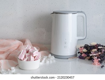 On The Countertop Of A Bright Marshmallow Kitchen Next To A White Electric Kettle And A Bouquet Of Flowers. Coffee Pause.