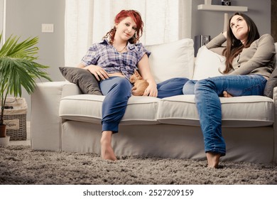 On a cozy sofa, while one woman reaches out beyond the frame with her eyes, her friend sits pondering quietly - Powered by Shutterstock