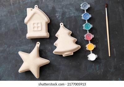 On A Dark Background Are Colored Paints, A Brush And Papier-mâché Figures In The Form Of A Star, A House, A Christmas Tree