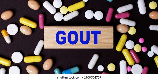 On a dark background, multi-colored pills and the word GOUT on a wooden block. Medical concept