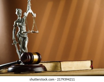 On A Dark Beige Background, A Bronze Figurine Of Themis, The Goddess Of Justice, A Wooden Judge's Gavel And A Book. Symbols Of A Fair Trial, The Rule Of Law.