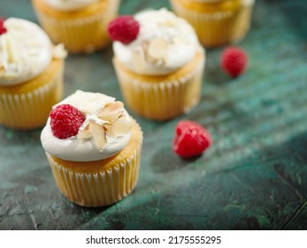 On A Dark Green Background, Sweet Muffins With Whipped Cream, Almonds And Raspberries. Lots Of Objects. Restaurant, Hotel, Cafe, Deli, Confectionery. There Are No People In The Photo.