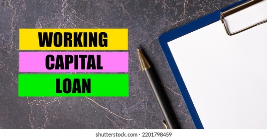 On A Dark Marble Background, A Tablet With Paper, Pen And Three Bright Multi-colored Strips Of Paper With The Text WORKING CAPITAL LOAN