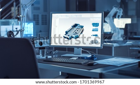 On the Desk Computer With CAD Software and Design of 3D Industrial Machinery Component. In the Background Robot Arm Concept Standing in Heavy the Dark.Industry Engineering Facility.