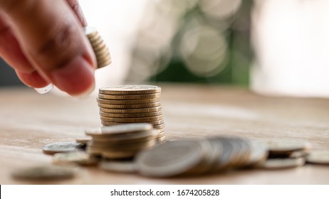 On the desk have coin pile and holding put down coin  on it. Concept Planning for spending and accumulating money Including paying taxes.
