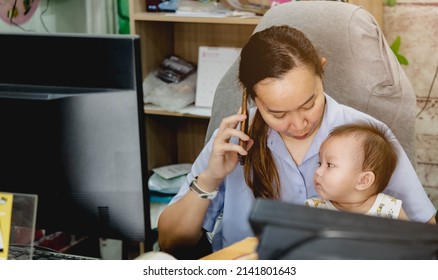 On The Desk In The House, Mom Talking On Mobile Phone Along With Carrying A Child,  Work Form Home  Concept.