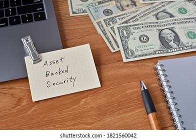 On The Desk There Are Bills, A Laptop, And Memos With The Word Asset Backed Security Written On It.