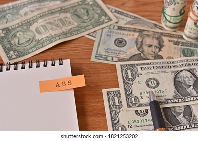 On The Desk There Are Bills, A Notebook, And A Sticky Note With The Word ABS Written On It. It Was An Abbreviation For The Financial Term Asset Backed Security.