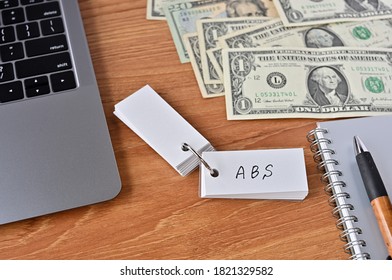 On The Desk There Are Bills, A Notebook, And A Sticky Note With The Word ABS Written On It. It Was An Abbreviation For The Financial Term Asset Backed Security.