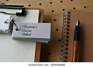 On The Desk There Is A Clipboard, A Notebook, And A Word Book With The Word Economic Value Added.