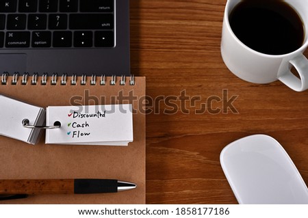 On the desk there is a laptop, a cup of coffee, and a word book with the word DCF written on it. It was an abbreviation for discounted cash flow.