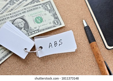 On The Desk Were Bills, A Notebook, And A Word Book With The Word ABS Written On It. It Was An Abbreviation For The Financial Term Asset Backed Security.