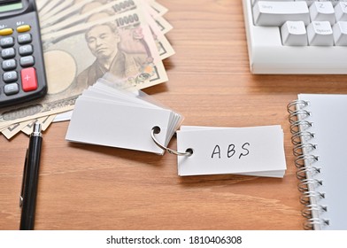 On The Desk Were Japanese Yen Bills, A Keyboard, A Notebook, And A Word Book With The Word ABS Written On It. It Was An Abbreviation For The Financial Term Asset Backed Security .