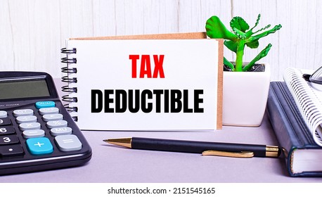On the desktop are a calculator, diaries, a potted plant, a pen and a notebook with the text TAX DEDUCTIBLE. Business concept. Workplace close up - Shutterstock ID 2151545165
