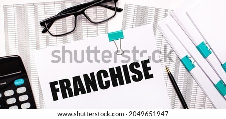 On the desktop are reports, documents, glasses, a calculator, a pen and paper with the text FRANCHISE. Business concept