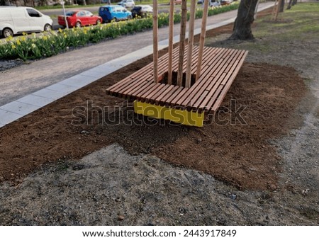 on the edge of the elevated terrace overlooking the park is a concrete long flowerpot with wood paneling and a rectangular bench. is part of the city promenade on the street and square
