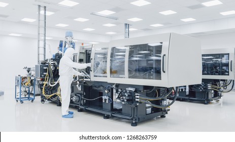 On A Factory Scientist In Sterile Protective Clothing Work On A Modern Industrial 3D Printing Machinery. Pharmaceutical, Biotechnological And Semiconductor Creating  Manufacturing Process.