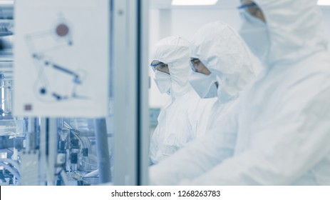 On A Factory Team Of Scientists In Sterile Protective Clothing Work On A Modern Industrial 3D Printing Machinery. Pharmaceutical, Biotechnological And Semiconductor Creating / Manufacturing Process.