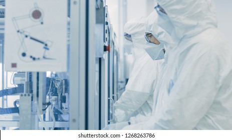 On A Factory Team Of Scientists In Sterile Protective Clothing Work On A Modern Industrial 3D Printing Machinery. Pharmaceutical, Biotechnological And Semiconductor Creating / Manufacturing Process.