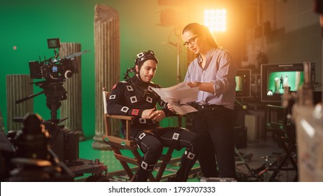 On Film Set: Prominent Female Director Explains Scene To Male Actor Wearing Motion Capture Suit And Playing Green Screen Scene In Superhero Movie. On Big Film Studio Professional Crew