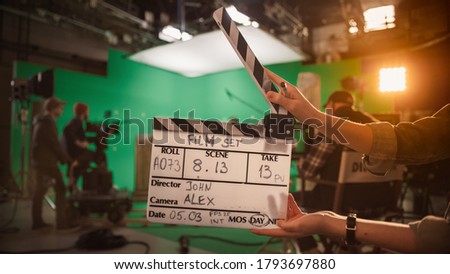 On Film Studio Set Camera Assistant Holds Clapperboard. Green Screen Scene with Talented Cameraman in the Background. Close-up Shot.