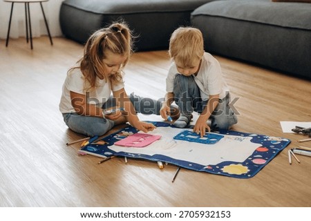 On the floor, learning how to draw. Little kids are playing together in the domestic room at daytime.
