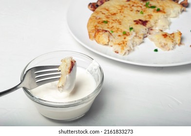 On Fork Is Piece Of Potato Tortilla - A Traditional Swiss Dish, The Fork Is Raised Over A Saucepan With Cream Sauce. In The Background, You Can See Part Of A Plate With Potato Pancake And Mushrooms.