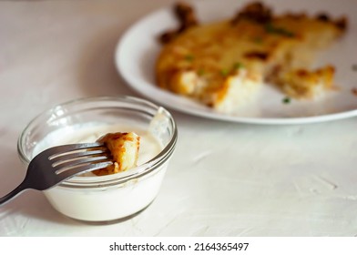 On Fork Is Piece Of Potato Tortilla - Swiss Dish, Fork Is Raised Over Saucepan With Cream Sauce. In Background, You Can See Part Of A Plate With A Potato Pancake, Side View, Natural Light Source.