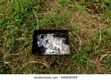 On the grass there is a barbecue with coals and ash.