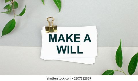 On A Gray Background - Green Leaves Of The Plant And A White Card Under A Gold Clip With The Text MAKE A WILL. Minimalist.