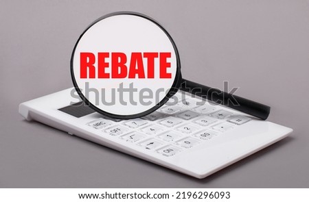 On a gray background, a white calculator and a magnifying glass with the text REBATE. Business concept