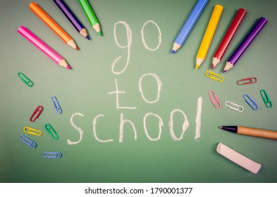 On a green chalkboard it is written to Go to school, next to it are crayons, pencils, colored paper clips, and a pen. Concept of the school, academic year. Beautiful, fun background for school.