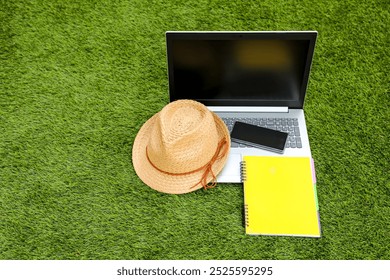 On the green grass on a summer day lies a laptop, a smartphone, a straw summer hat and a notebook. Series "Digital Nomads". - Powered by Shutterstock