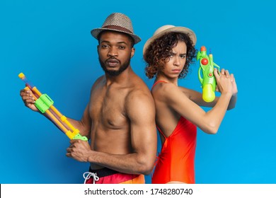 On Guard Of Summer Fun. Serious black couple in swimwear holding water guns, posing over blue studio background, free space