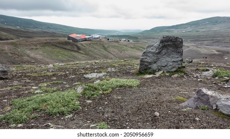 On the hills with sparse vegetation there are houses of the tourist base. Cloudy. In the foreground is a large picturesque boulder. Kamchatka