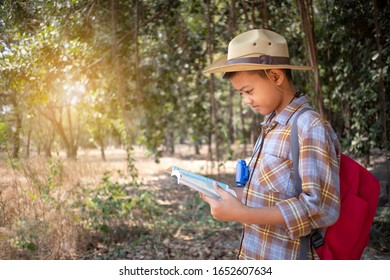 On Holidays, Asian Boys Aged 6 To 8 Years Wear A Red Backpack. Wearing A Long Sleeved Shirt. Are Doing Long-distance Activities For Outdoor Adventures In The Forest, Outdoor Adventure Concept