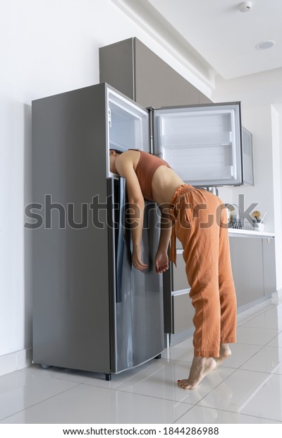 On a hot day, the girl cools with his\
head in the refrigerator. Broken air\
conditioner.