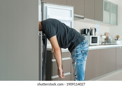 On a hot day, the guy cool down with his head in the refrigerator. Broken air conditioner. - Shutterstock ID 1909114027