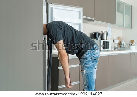 On a hot day, the guy cool down with his head in the refrigerator. Broken air conditioner.