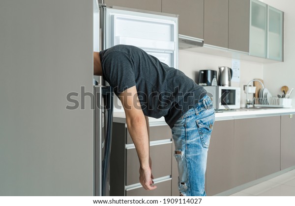 On a hot day, the guy cool down\
with his head in the refrigerator. Broken air\
conditioner.