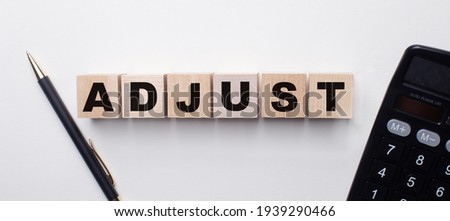 On a light background between the calculator and the pen there are wooden cubes with the word ADJUST. Financial concept