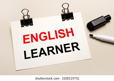 On A Light Background, A Black Open Marker And On Black Clips A White Sheet Of Paper With The Text ENGLISH LEARNER