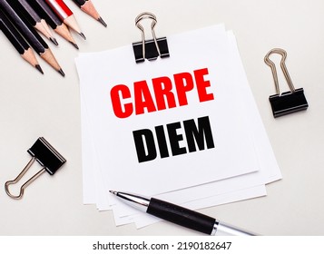 On a light background, black pencils, black paper clips, a pen and a sheet of white paper with the text CARPE DIEM