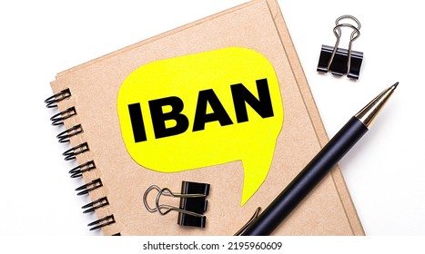 On A Light Background, A Brown Notebook, A Black Pen And Paper Clips, And A Yellow Card With The Text IBAN International Bank Account Number