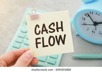 On A Light Background - Cash, A White Calculator And A Yellow Sticker Under A Black Paper Clip With The Text CASH FLOW. Business Concept